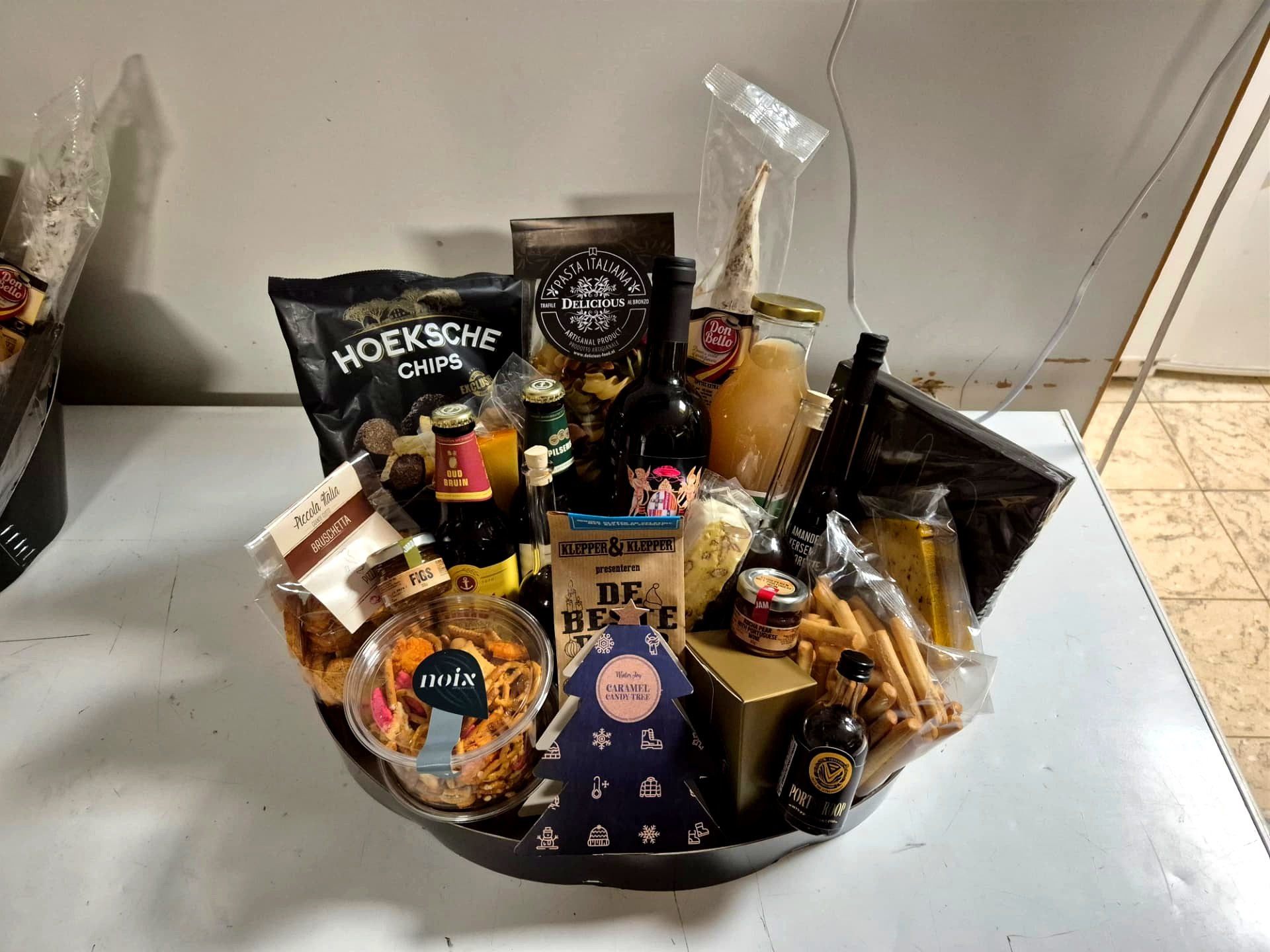 Kerstpakket met bier, wijn, chips, pasta en zoetigheid in een zwarte schaal
