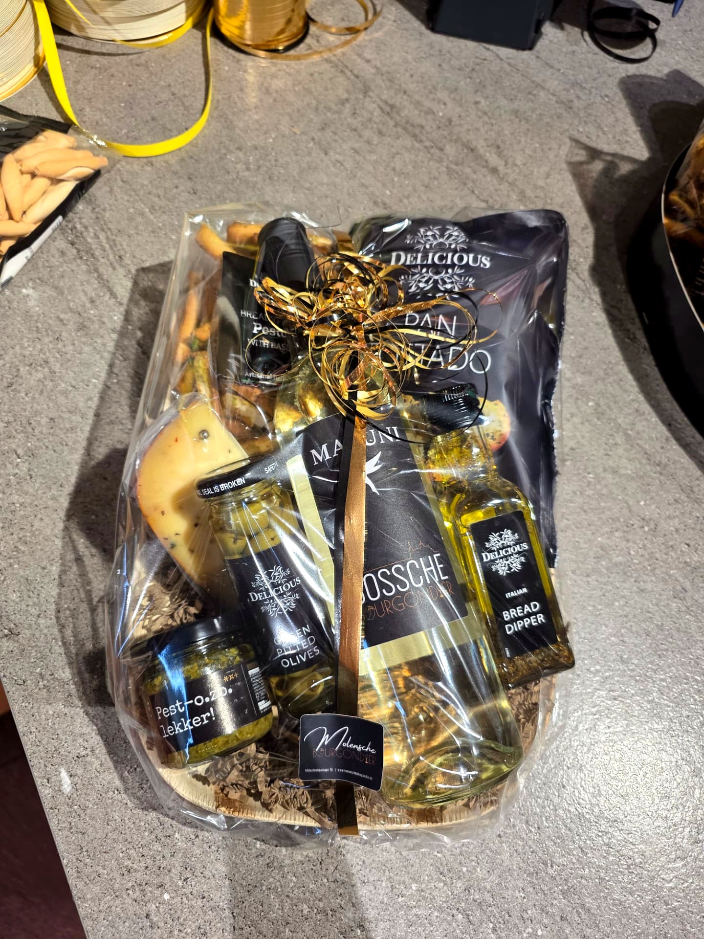 Feestelijk ingepakt geschenkpakket met wijn, kaas, pesto en olijven